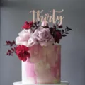 Primer plano del detalle del cake topper Thirty de acrílico oro rosa, elegante decoración floral. - Treinta / Rosa oro