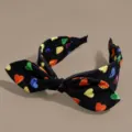 Vista dettagliata di un cerchietto in tessuto nero con cuori colorati stampati e nodo elegante. - Nero con Cuori Colorati