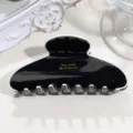 Close-up detail of a glossy black and white acetate hair claw clip with gold stamped text. - Medium Crescent - White Edge Black