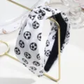 Close-up of a wide knotted fabric headband with a classic black and white soccer ball print. - White