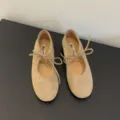 Close-up view of beige suede ballet flats with delicate lace-up bow design and soft sole. - 35 / Apricot