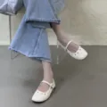 Gros plan de chaussures plates Mary Jane blanches élégantes avec détails ajourés et bride. - Abricot