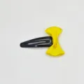 Detail shot of a bright yellow ribbon bow attached to a classic black metal snap hair clip. - Yellow