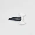 Close up detail of a cute black metal BB hair clip decorated with a clean white bow ribbon. - White