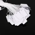 White blank paper hang tags with strings for pricing and labeling, ideal for retail items. - 2.3cm x 1.3cm
