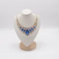 Detail of gold necklace with vivid blue teardrop crystals and sparkling clear rhinestones. - M / Beige