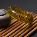 Close-up view of a transparent green synthetic amber resin bangle bracelet on bamboo mat. - Green Tea Amber