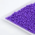 Close-up detail of vibrant purple glass seed beads displayed on a white tray, ideal for DIY crafts. - Purple
