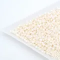 Close-up of milky white glass seed beads in a white tray, perfect for DIY jewelry making. - Beige