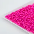 Close-up of vibrant hot pink glass seed beads in a white tray, perfect for DIY jewelry making. - Rose Red