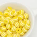 Close-up of yellow and white striped resin beads in a bowl for DIY crafts and jewelry making. - Yellow