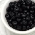 Close-up detail of glossy black wheel spacer beads in a white bowl for DIY jewelry making accessories. - Black