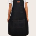 Denim work apron with practical pockets and chest logo patch, ideal for kitchen and styling use. - Blue