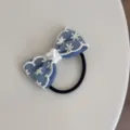Close-up detail of blue denim bow hair tie with white lace embroidery and heart bead. - Heart Hair Tie
