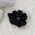Detalle de coletero de satén negro, elegante accesorio para el cabello de mujer, diseño liso. - Coletero Negro