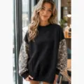 Detailed close-up view of the casual black sweatshirt with trendy contrast camo sleeves indoors. - S / Black