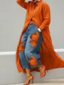 Gedetailleerd overzicht van het lange oranje vest gecombineerd met hippe bloemenjeans. - Oranje