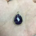 Detailansicht eines tropfenförmigen violetten Steinanhängers mit Zirkonrand in Goldoptik. - Amethyst