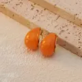 Detailed close-up of trendy orange teardrop earrings with gold trim on textured stone surface. - Orange