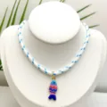 Gros plan détaillé d'un collier pendentif poisson émaillé coloré avec un cordon rayé. - Pendentif avec chaîne (comme sur la photo) (Q01-20) / Rayé Blanc Bleu