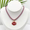 Primer plano detallado del collar con colgante ovalado vintage y patrón floral rojo. - Colgante Floral Ovalado Con Cordón Granate