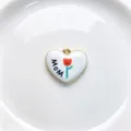 Close-up detail of a white enamel heart pendant featuring a cute tulip and MOM lettering. - Tulip MOM Style (C01-9)