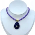 Close-up of the carved deep blue teardrop gemstone pendant with zircon and gold rings on purple cord. - Pendant With Chain / Purple
