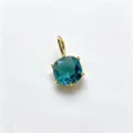 Close-up view of a cushion cut teal blue zircon pendant in a polished gold tone setting accessory. - F-09 Lake Blue