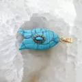 Vue détaillée du pendentif poisson turquoise avec une bélière dorée sur fond de cristal. - Turquoise