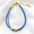Primo piano di un bracciale in corda blu fatto a mano con perle dorate su raso bianco. - 07# (Azzurro)