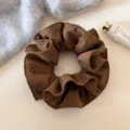 Bruine stoffen haarelastiek detailshot op schone witte ondergrond met gebreide stof als rekwisiet. - Slanke Taille Stijl Scrunchie / Koffie