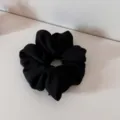 Detailed close-up of a classic black satin scrunchie, soft fabric texture and pleated design. - Black