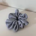 Detailed view of a light grey satin hair scrunchie, soft pleated texture for everyday wear. - Blue