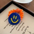 Primo piano dettagliato di un elastico per capelli blu con faccina sorridente e tessuto arancione. - Arancione