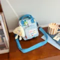 Light blue canvas crossbody bag with cute plush pendant and vibrant geometric patterns. - Blue + Cheese Pendant