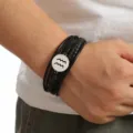 Detail shot of the multi-layer braided leather bracelet featuring a silver Aquarius zodiac charm on the wrist. - Aquarius
