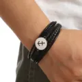 Detailed close-up of a multi-layer black braided leather bracelet featuring a steel zodiac charm. - Sagittarius