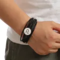 Close-up view of men's multi-layer braided leather bracelet featuring a metal zodiac sign charm. - Leo