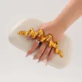 Detail shot of a stylish clutch bag featuring a bold gold wavy metal handle and cream PU body. - Off White