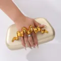 Detail shot of gold clutch bag featuring unique metallic wave handle for stylish evening wear. - Gold