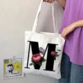 Primo piano dettagliato di borsa tote in tela bianca con grande lettera M nera e stampa floreale. - Lettera M / 15x13