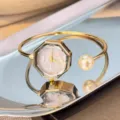 Detalle de un elegante reloj de pulsera dorado con esfera octagonal y un hermoso acento de perla. - Dorado