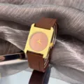 Detailansicht der quadratischen Damen Quarzuhr mit goldenem Gehäuse und braunem Silikonarmband. - Braun