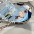 Detail view of women rose gold rhinestone heart quartz watch with elegant clover crystal bracelet. - Coffee