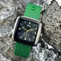 Nahaufnahme einer quadratischen Quarzuhr mit grünem Silikonarmband und schwarzem Zifferblatt. - Grün