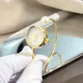 Goldfarbene Quarz-Spangenuhr mit Perlenakzent und Zifferblatt mit Strasssteinen für Damen. - Perlmutt-Zifferblatt / Gold