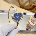 Nahaufnahme der eleganten goldenen Herz-Armreif-Uhr mit Perlenakzent und blauem Zifferblatt. - Herz Blaues Zifferblatt / Gold
