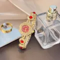 Goldene Quarz-Armbanduhr Detailansicht mit Sonnenblumen-Zifferblatt und roten Schmucksteinen. - Rot