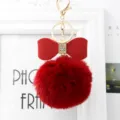 Close-up view of the red fluffy fur ball keychain with a rhinestone bow and gold hardware. - 8cm Pompom / Burgundy