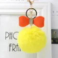 Close-up view of the fluffy yellow pom-pom keychain featuring an orange leather bow. - 8cm Pompom / Yellow